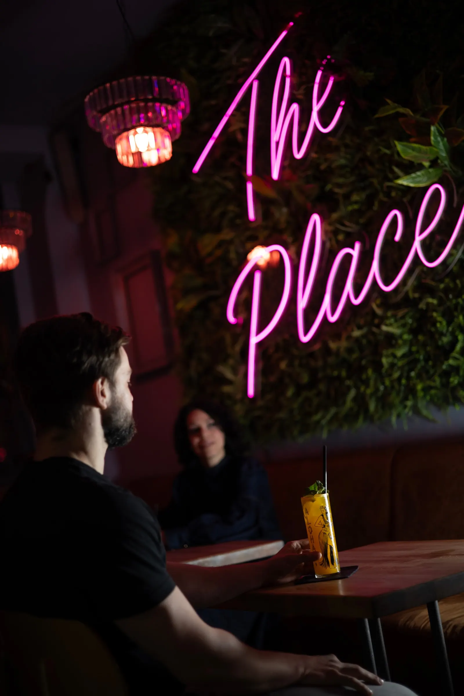 Hosté u baru The Place pod neonovým nápisem