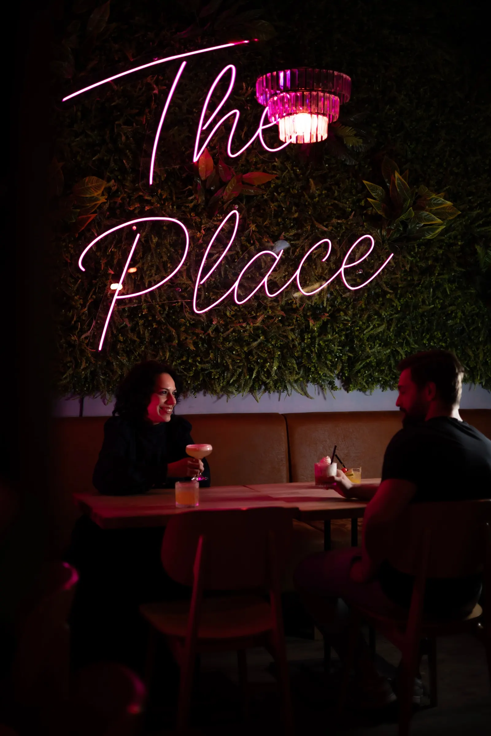 Interiér baru The Place — neon na zelené stěně a posezení